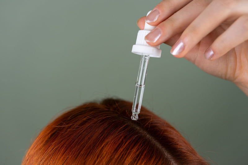 Femme aux cheveux roux appliquant une huile capillaire, soin pour préserver l'éclat des cheveux colorés