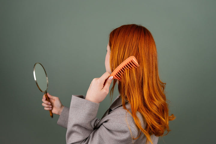 Femme qui se coiffe face à un petit miroir, retouche coiffure en journée avec une brosse de poche