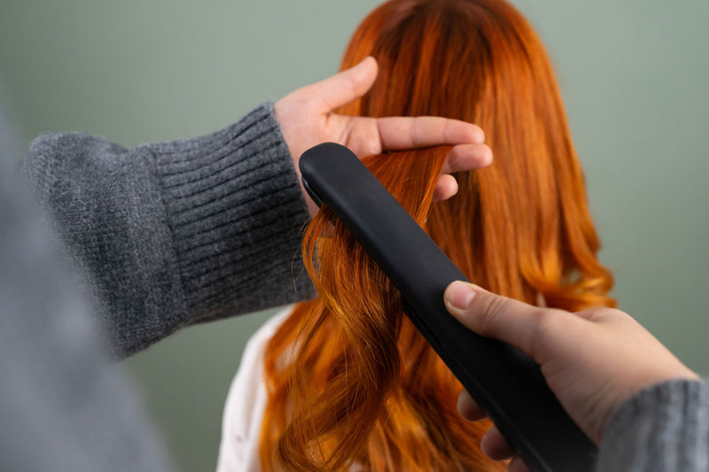 Coiffeuse lissant une mèche de cheveux longs au fer plat pour un effet lisse et brillant glass hair