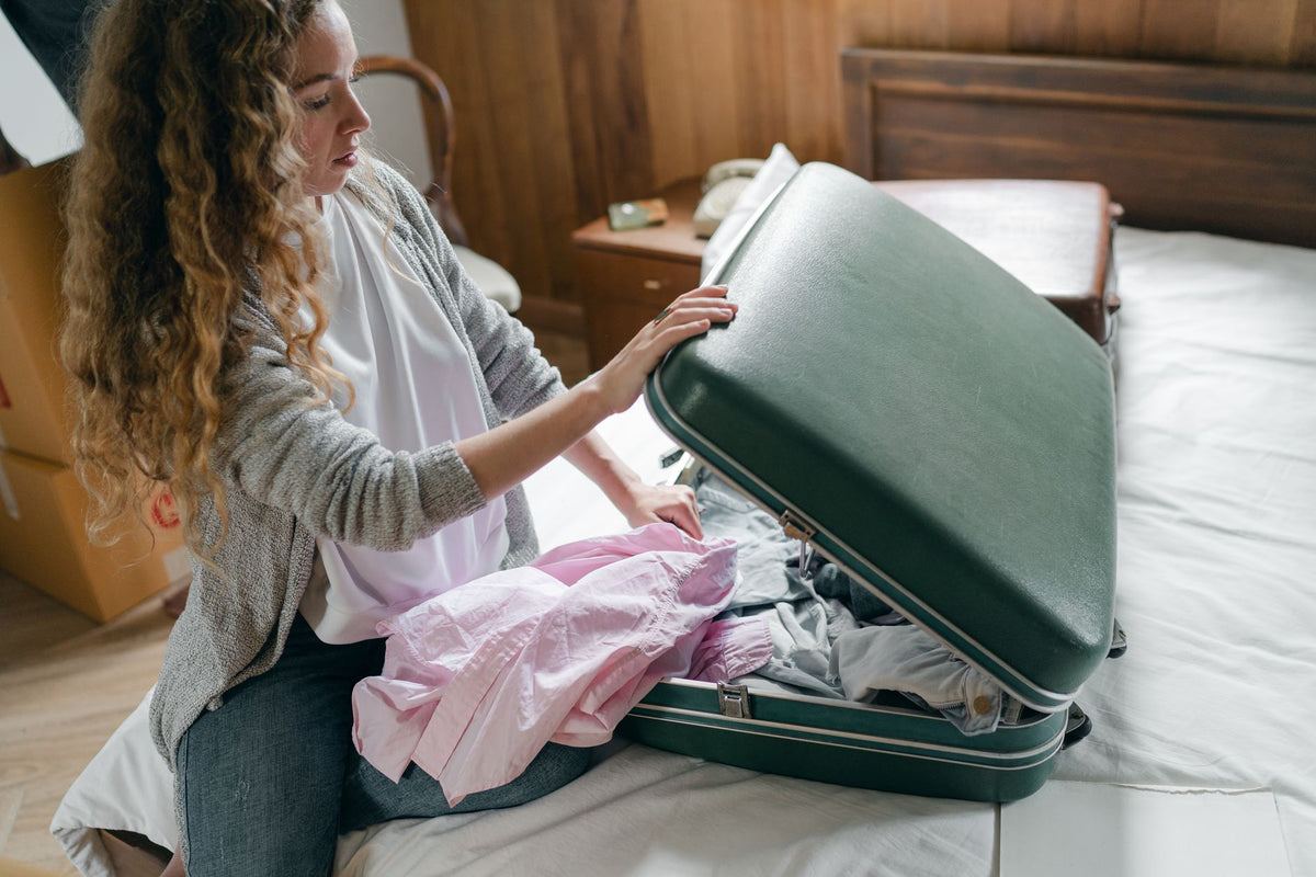 Femme aux cheveux bouclés préparant sa valise avant un voyage, routine capillaire indispensable
