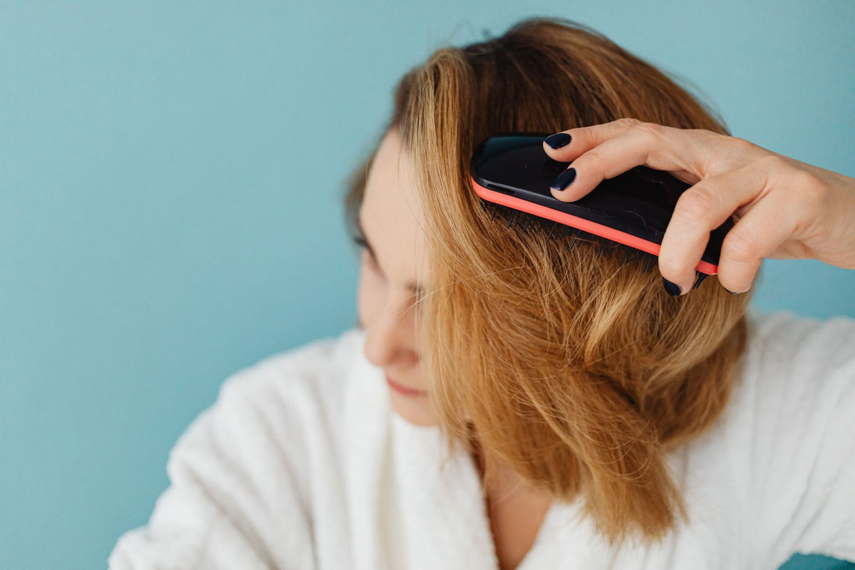 Femme en peignoir se brossant délicatement les cheveux pour éviter la casse