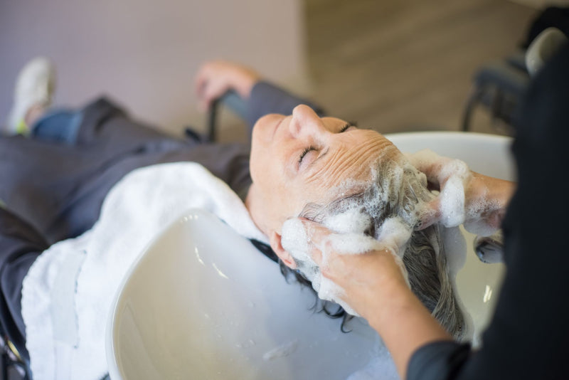 Femme se faisant masser le cuir chevelu pendant le shampoing, routine douce contre les pellicules